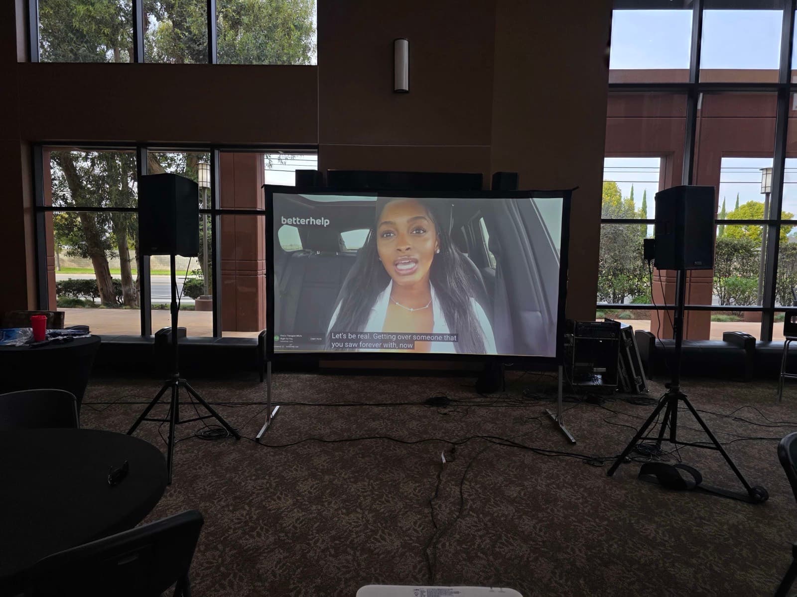 A 4,300-lumen projector and PA speakers set up in a bright, window-lined venue in Orange County, with the projected image still clearly visible in daylight