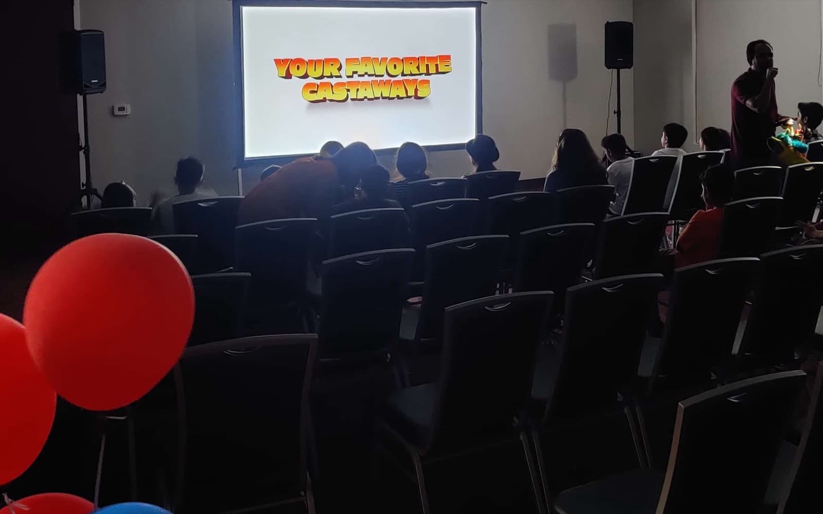 Powered PA speakers on stands and a wireless microphone in use at an indoor community hall screening in Orange County